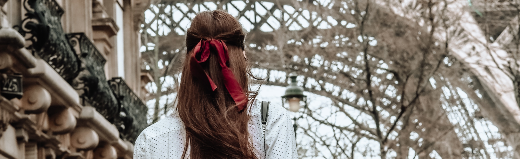 Eine Frau mit roter Schleife im Haar steht mit dem Rücken zur Kamera nah am Eifelturm.